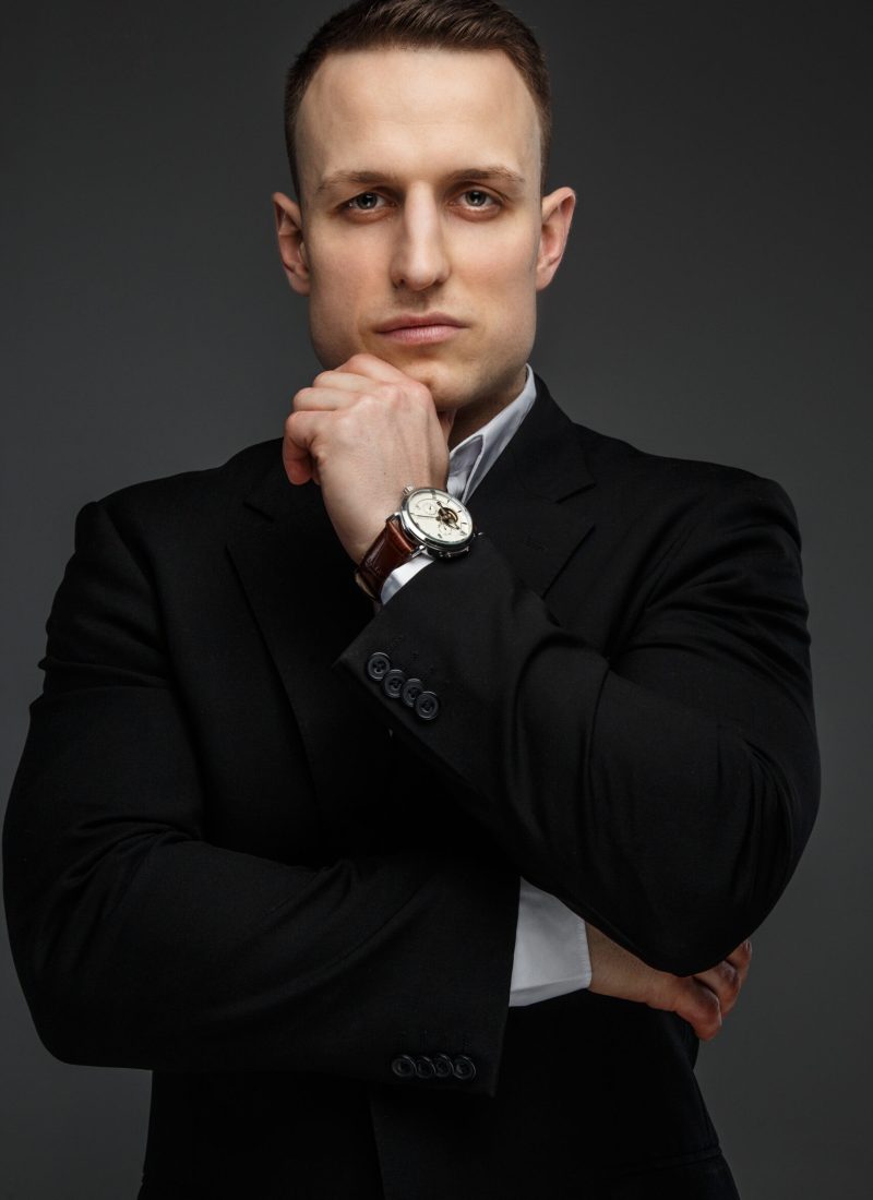 Portrait of successful business man in a black suit on grey background.