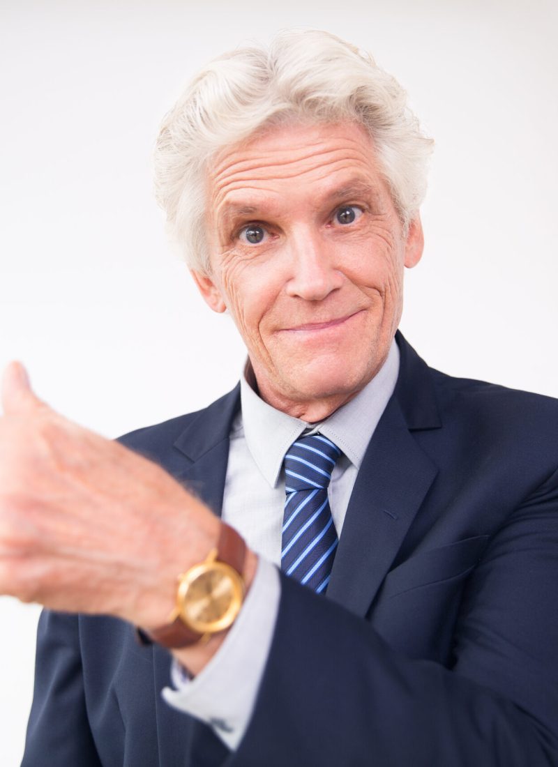 Studio portrait of surprised senior Caucasian businessman wearing suit showing direction, looking at camera and smiling